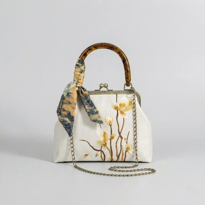 The beige embroidered kiss-lock bag shown with its detachable gold chain strap for crossbody wear.