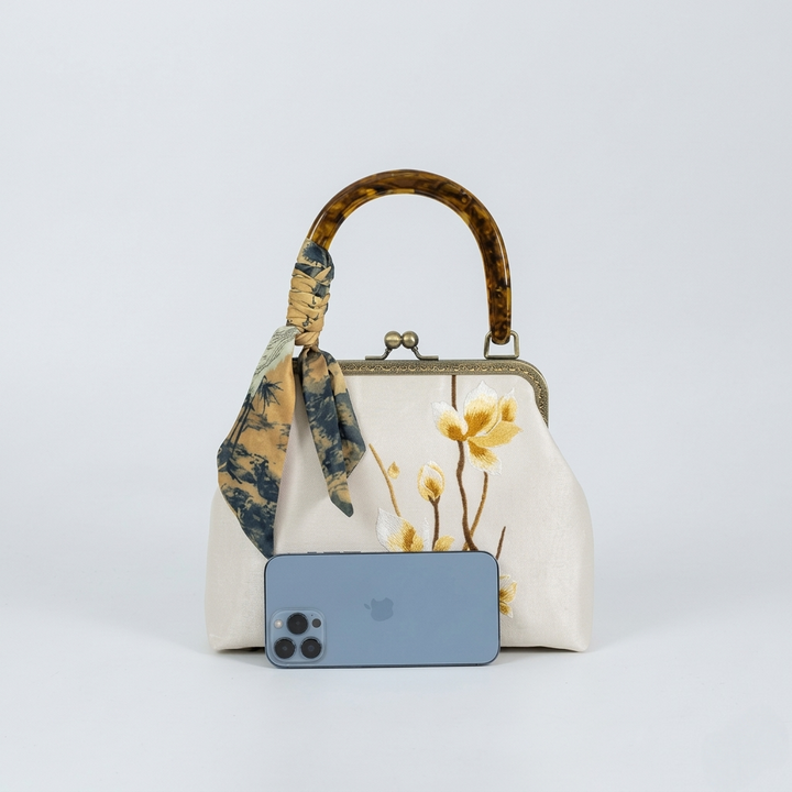 Size comparison of the beige doctor bag style handbag next to a smartphone to show its practical dimensions.