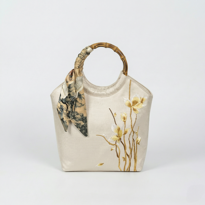 Side perspective of the beige embroidered tote, highlighting the silk scarf detail on the bamboo ring handle.
