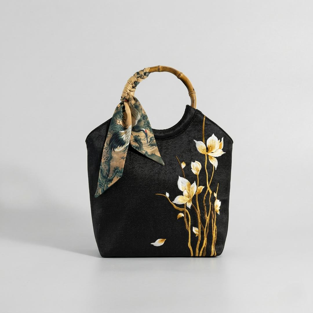 Angled view of the black Chinoiserie tote bag showcasing the intricate golden flower embroidery and silk scarf handle.