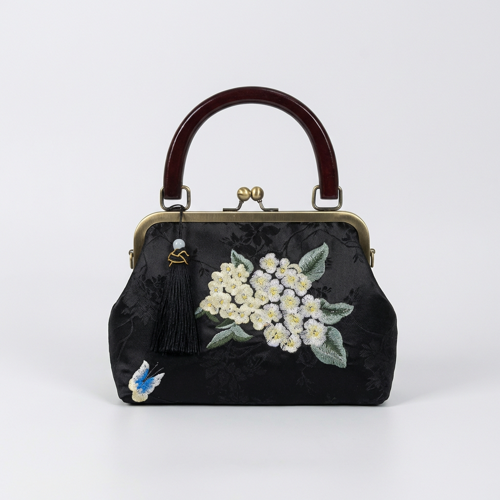 Classic black silk handbag with artisanal white floral embroidery and a timeless kiss-lock design.
