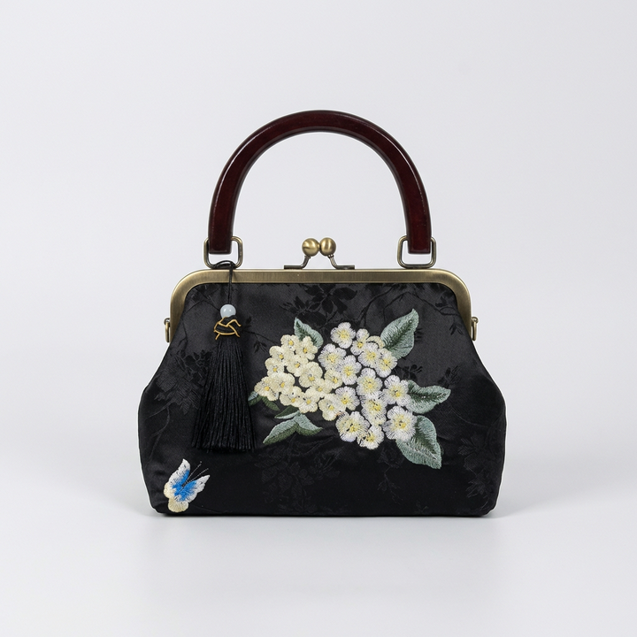 Classic black silk handbag with artisanal white floral embroidery and a timeless kiss-lock design.