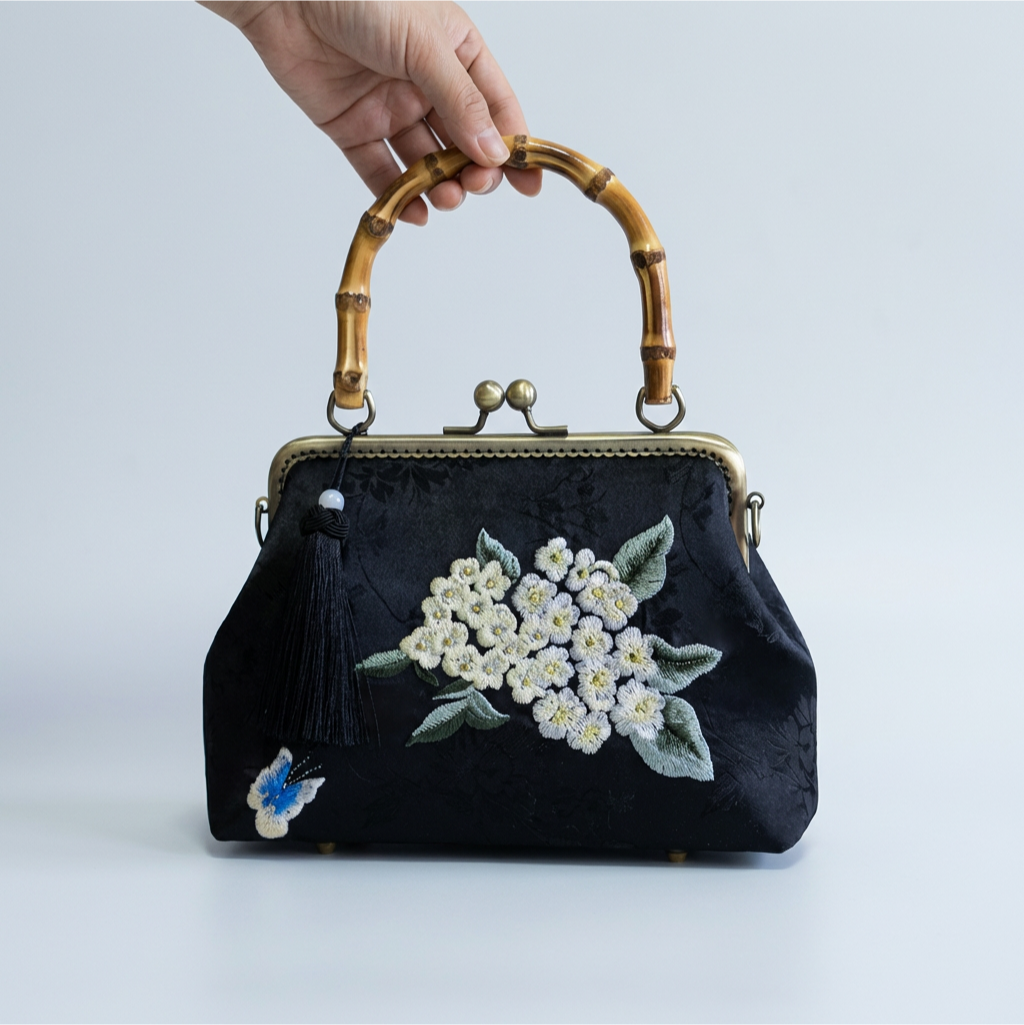A person holding the black silk embroidered purse with a bamboo handle, demonstrating its compact and elegant size.