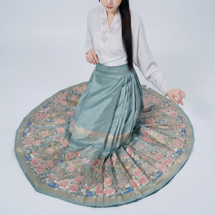 A top-down view of the pleated skirt spread out in a circle, showcasing its full volume and the beautiful artistic floral border at the hem.