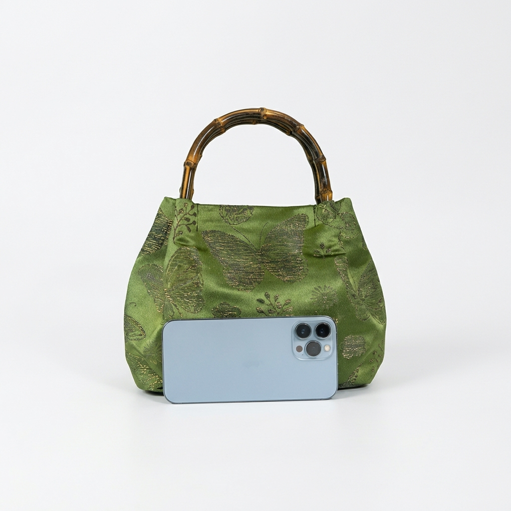 Size comparison of the green bamboo satchel next to a smartphone to demonstrate its practical daily capacity.