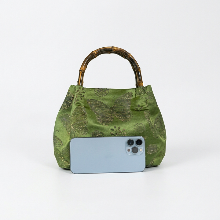 Size comparison of the green bamboo satchel next to a smartphone to demonstrate its practical daily capacity.
