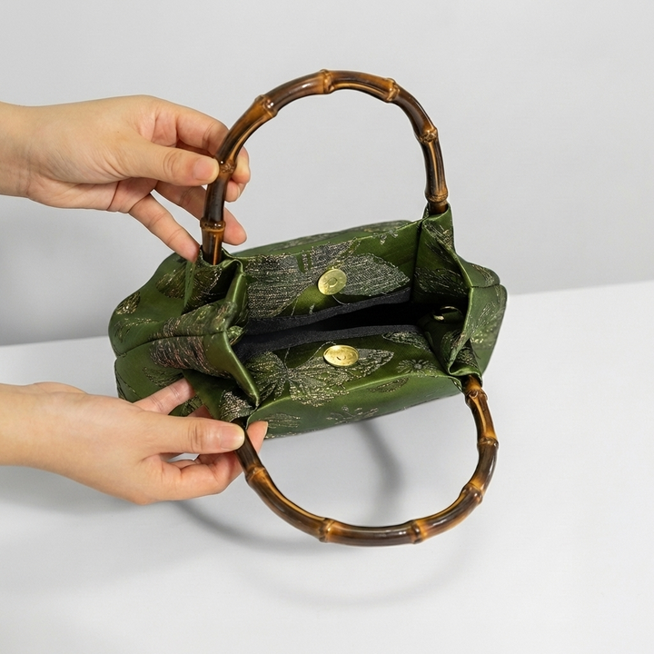 Demonstrating the opening of the green bamboo brocade satchel to show interior accessibility.