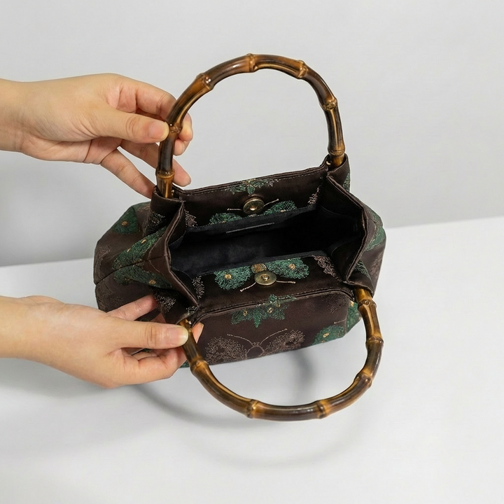 Opening the maroon bamboo handle satchel by hand to showcase its capacity for everyday items.